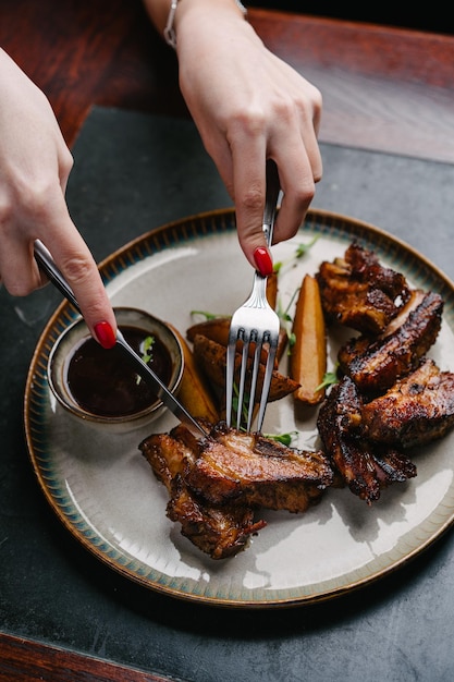 Vrouw neemt gegrilde varkensribbetjes met gebakken aardappelen en BBQ-saus Close-up