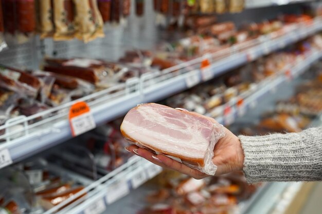 Foto vrouw neemt verpakt varkensvlees van de plank in de supermarkt