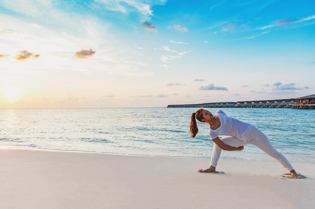 Vrouw oefent op het strand tegen de hemel tijdens de zonsondergang