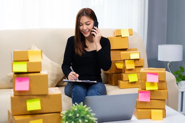 Vrouw ondernemer praten met de klant op een mobiele telefoon en het schrijven van productbestelling thuis kantoor