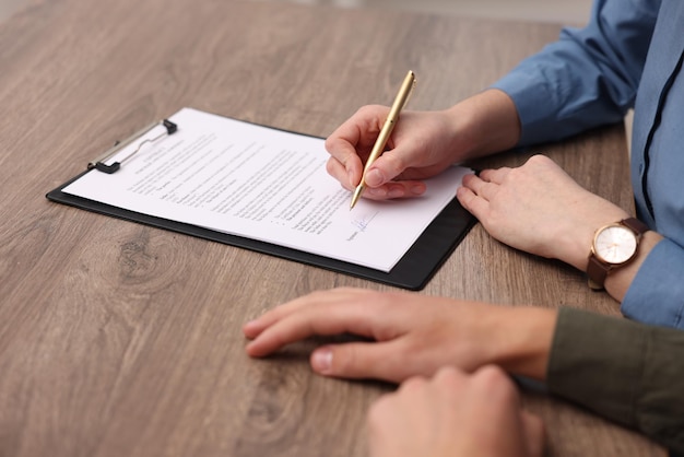 Vrouw ondertekent een document bij een houten tafel