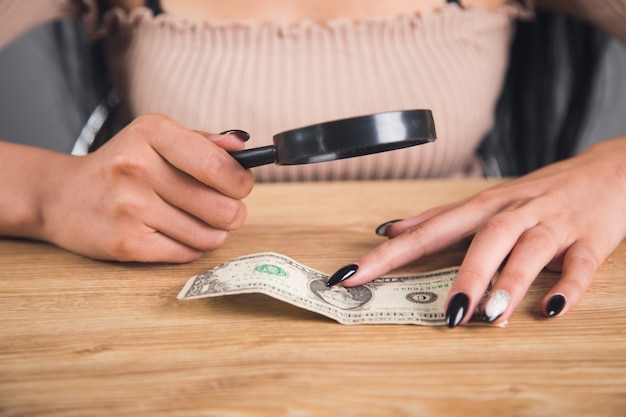 Vrouw onderzoekt het geld met een vergrootglas. vals cheque concept