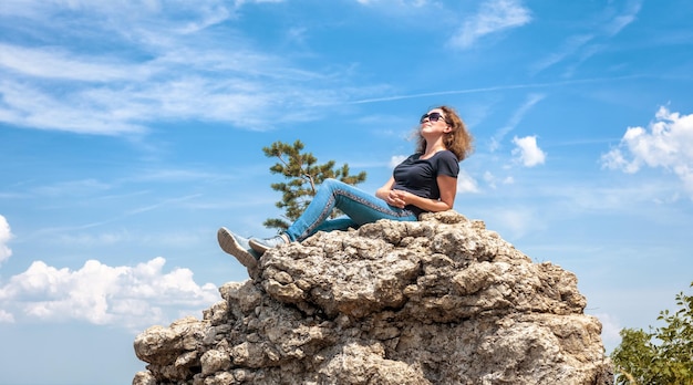 Vrouw ontspannen op de bergtop in de zomer Gelukkig mooi persoon zonnebaden op klif Vrij volwassen meisje rusten na een wandeling in de natuur op de blauwe hemelachtergrond