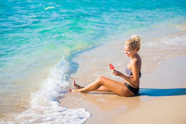 Vrouw ontspannen op het strand op een zomerse dag lachend met een plakje watermeloen in haar hand