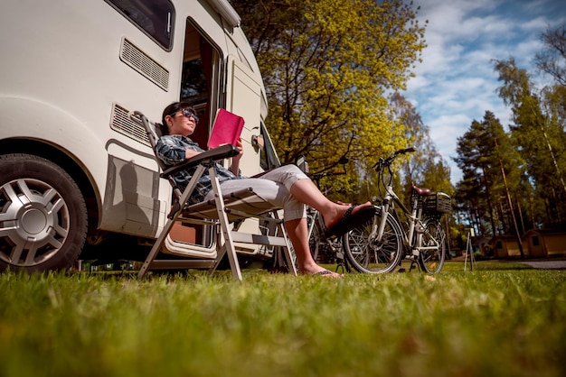 Vrouw ontspant en leest een boek in de buurt van de camping. Caravan auto vakantie. Familie vakantiereizen, vakantiereis in camper RV.