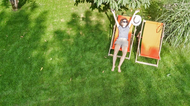 Vrouw ontspant in de zomertuin in zonnebank strandstoel op gras, jong meisje buiten in groen park