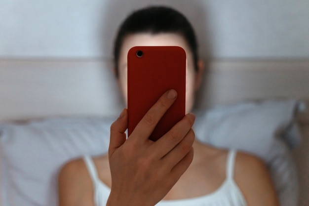 Vrouw op bed die 's avonds laat naar smartphone kijkt.