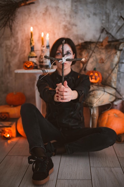 Vrouw op de achtergrond van feestelijke Halloween-versieringen met een houten kruis