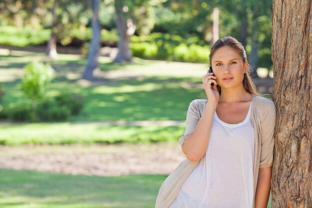 Vrouw op de cellphone die tegen een boom leunt