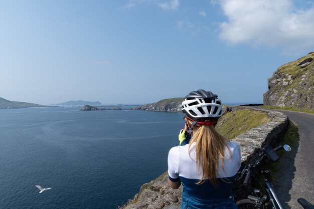 Vrouw op de fiets maakt foto's met haar mobiele telefoon van kliffen op het schiereiland Dingle Ir