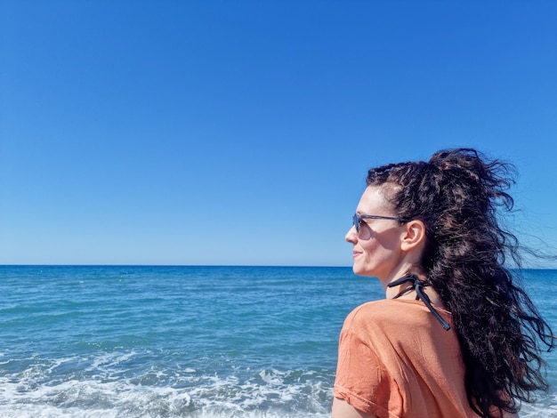 Vrouw op de voorgrond die naar de horizon kijkt met het strand op de achtergrond