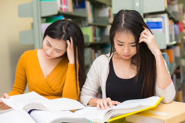 Vrouw op de voorgrond leest boeken. De jonge Aziatische Vrouw leest in de bibliotheek.