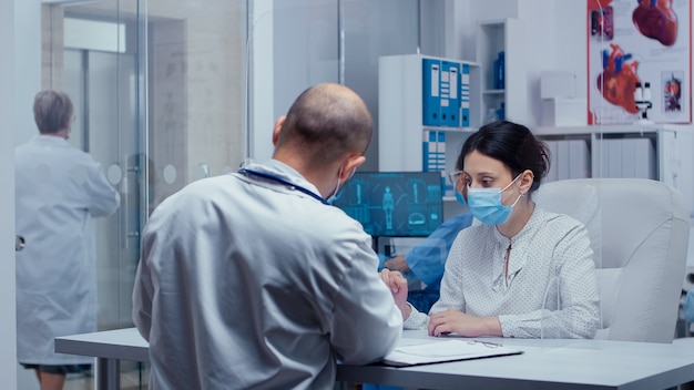 Vrouw op doktersafspraak tijdens COVID-19 met een masker en handschoenen, pratend met dokter door een beschermende muur. Medisch consult in concept van beschermende uitrusting, shot van sars-cov-2 global heal