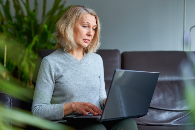 Vrouw op een bank die zich thuis concentreert aangezien zij aan laptop werkt.