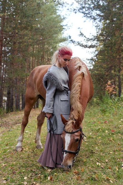 Vrouw op een paard in de herfst. Creatieve felroze make-up op het gezicht van het meisje, haarkleuring. Portret van een meisje met een paard. Paardrijden in het herfstbos. Herfst kleding