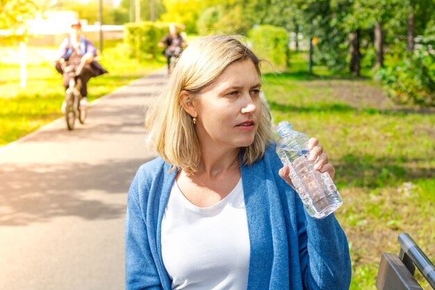 Vrouw op een zonnige warme dag die een fles vasthoudt terwijl ze water gaat drinken in het park