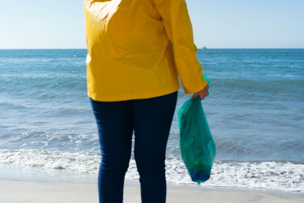 Vrouw op haar rug met een plastic zak vol afval op het strand