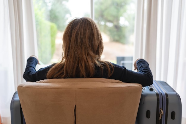 Vrouw op haar rug zittend in een leunstoel en met twee koffers rustend bij aankomst in haar vakantieappartement