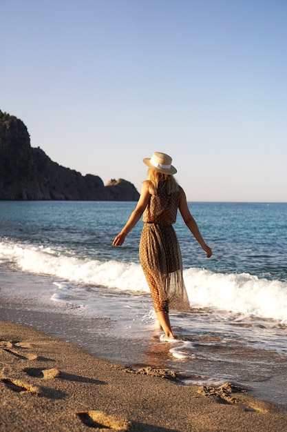 Vrouw op het strand in een bruine jurk en met een strohoed op vakantie op het strand