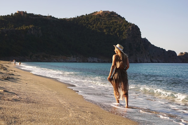 Vrouw op het strand in een bruine jurk en met een strohoed op vakantie op het strand