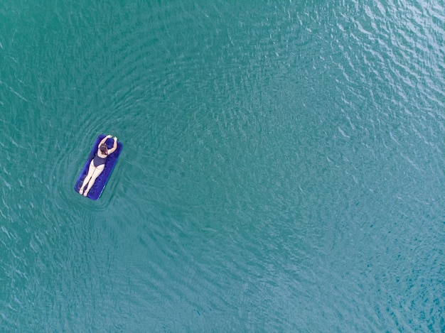 Vrouw op matras in azuurblauw water bovenaanzicht kopieerruimte