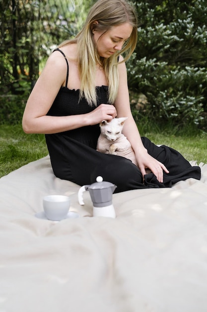 Vrouw op picknick met sfinx witte kat op deken in de tuin