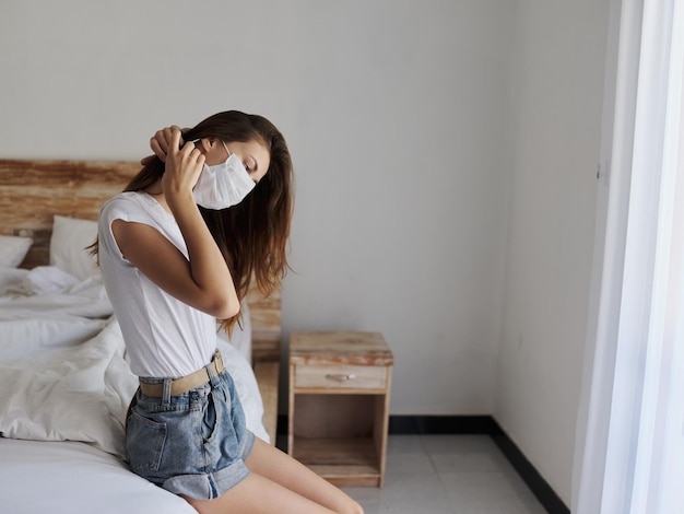 Vrouw op vakantie met medisch masker op haar gezicht zit op bed in geïsoleerde kamer