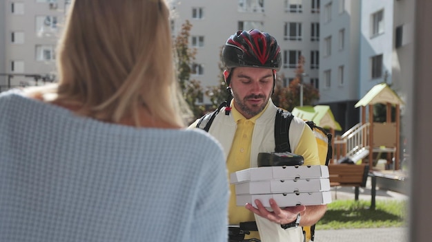 Vrouw open deur voor een pizzabezorger op een fiets met gele thermische rugzak met POS draadloze terminal voor smartphone betalen en ontvangt kartonnen dozen pizza Voedselbezorgingsconcept