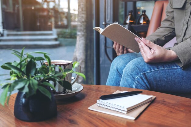 vrouw openen van een boek met laptops en koffiekopje op houten tafel in café
