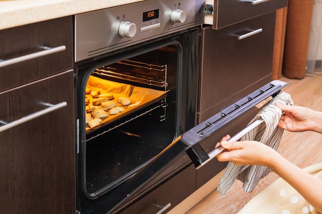 Vrouw opent de oven waar koekjes worden gebakken voor Halloween.