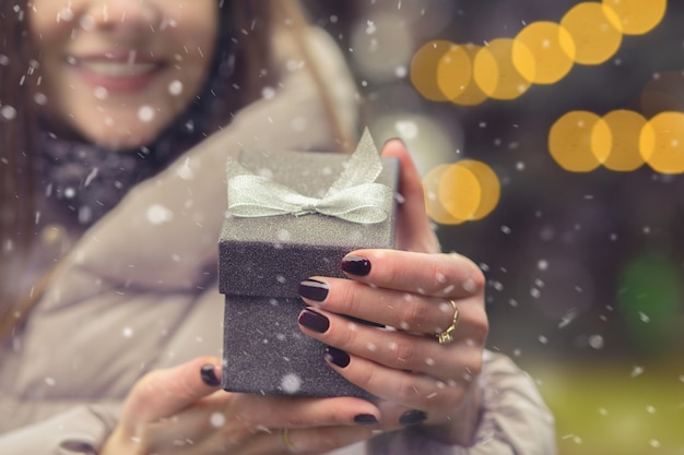 Vrouw opent een kleine geschenkdoos met een strik op straat met bokehlicht tijdens de sneeuwval