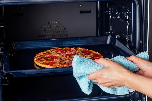 Vrouw opent ovens en neemt pizza met tomaten, olijven, champignons en kaasworst