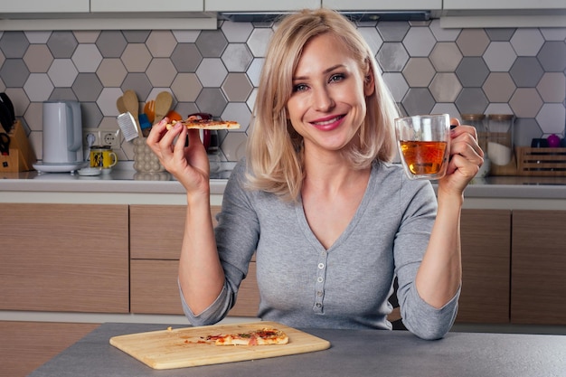 Vrouw opent ovens en snijd pizza met tomaten, olijven, champignons en kaasworst op een blauwe achtergrond in de studio