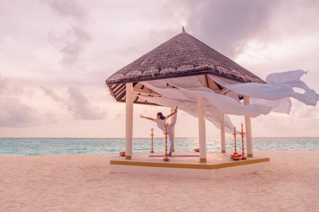 Vrouw opleiding yoga op het strand bij zonsondergang onder strandhut. Traditionele yogaplaats zachte pasteltinten