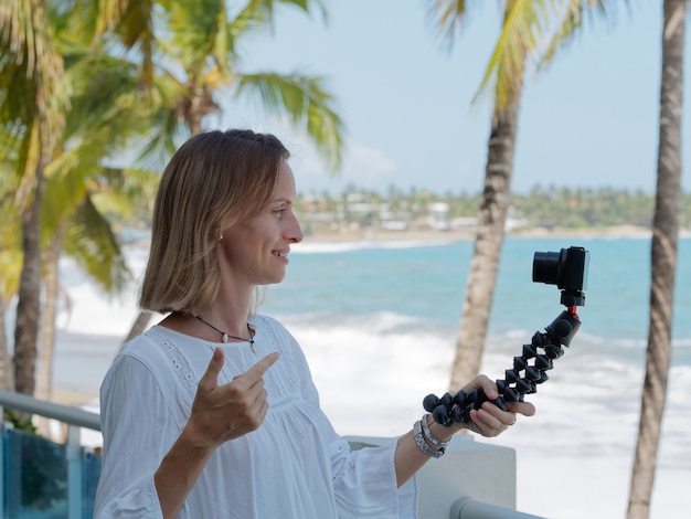 Vrouw opname reisblog op het strand. Oceaan en palmen boom achtergrond.