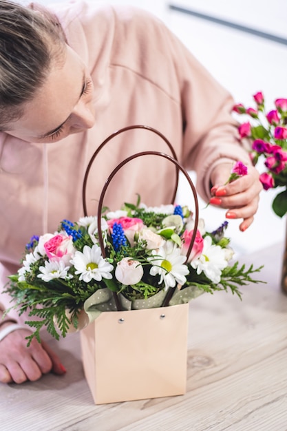 Vrouw oppakken van boeket van verschillende bloemen in papieren cadeauzakje met handvatten. Verticaal