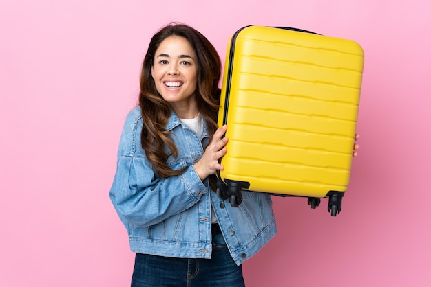 Vrouw over geïsoleerde blauwe muur in vakantie met reiskoffer en verrast