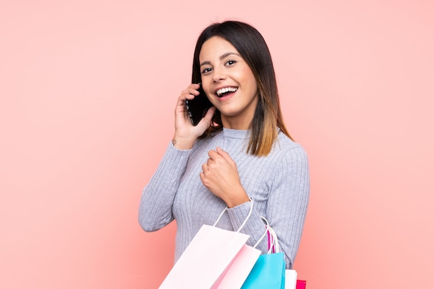 Vrouw over geïsoleerde roze muur met boodschappentassen en een vriend bellen met haar mobiele telefoon