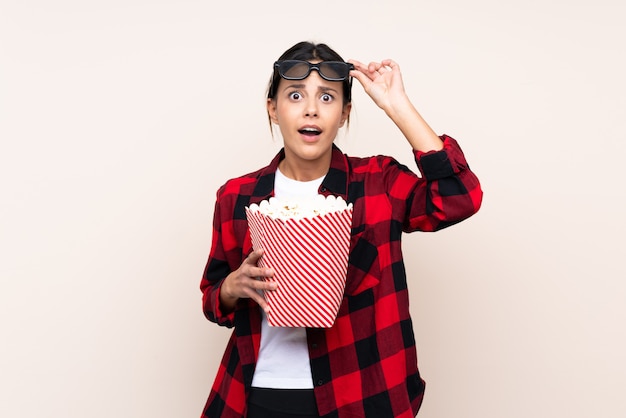 Vrouw over muur verrast met 3d glazen en het houden van een grote emmer popcorns
