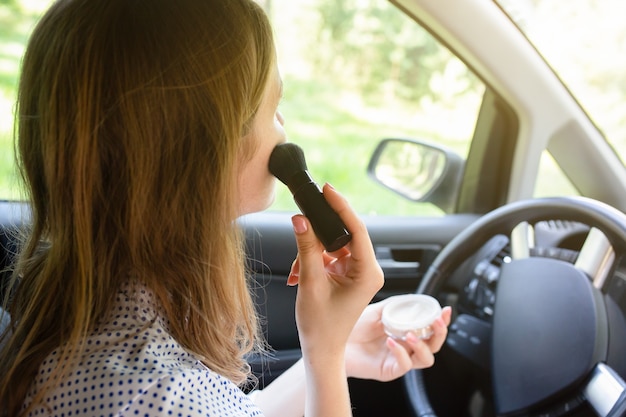 Vrouw past make-up toe in de auto. Meisje met gezichtspoeder achter het stuur. Gevaarlijke situatie op de weg. Kans op ongeval.