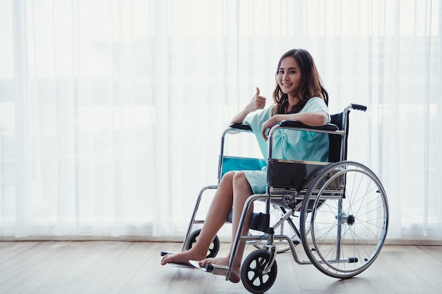 Vrouw patiënt in groen shirt zittend op de rolstoel van de ziekenhuiskliniek in de kamer van de patiënt. Jonge vrouwelijke patiënt herstelt in een ziekenhuiskamer vanwege ziekte.