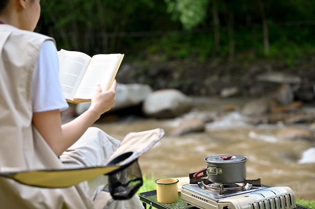 Vrouw picknickt en kampeert op de natuurlijke camping, leest een boek bij de rivier