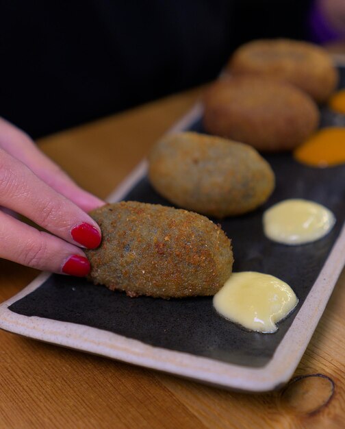 Vrouw plukt met de hand een kroket van een bord met sauzen