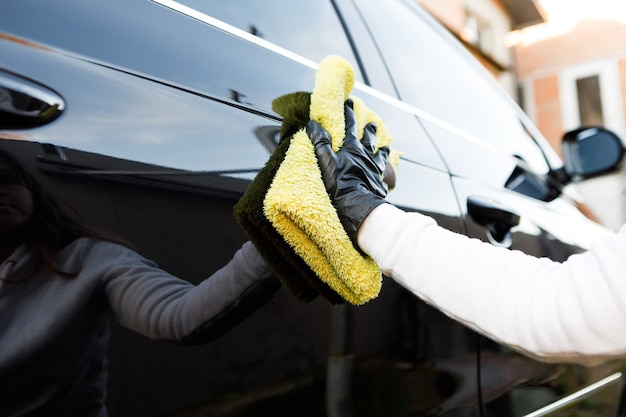 Vrouw poetst de auto met een microvezeldoek en polijst om de carrosserie van de auto af te vegen met poetsmiddel