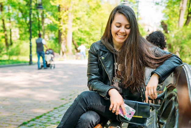 Vrouw portret glimlachend jonge volwassene zittend op een bankje in het park met behulp van phone