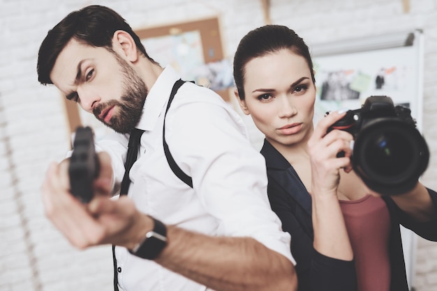 Vrouw poseert met camera, man poseert met pistool.