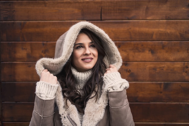 Vrouw poseren en houden kap terwijl je voor houten muur staat bij koud weer.