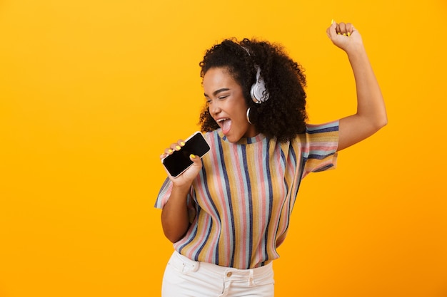 Vrouw poseren geïsoleerd over gele ruimte luisteren muziek met koptelefoon dansen zingen.