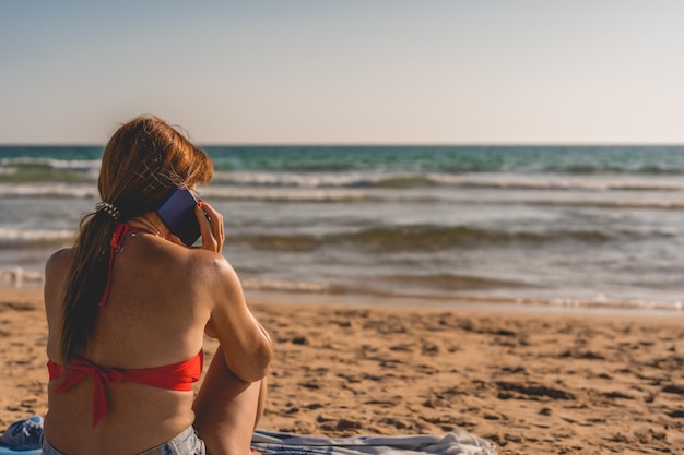 Vrouw praat op haar mobiele telefoon terwijl ze op het strand zit