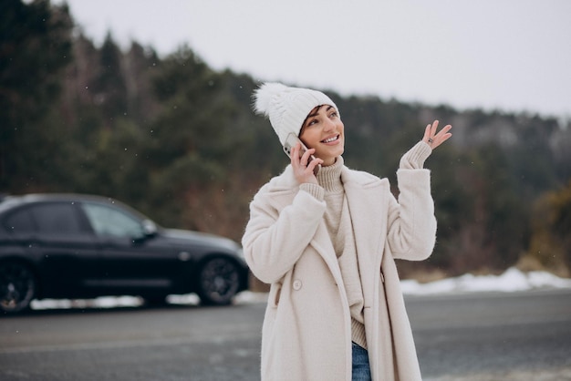 Vrouw praten aan de telefoon bij haar auto in winter forest